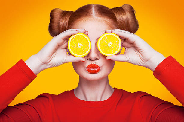 Young beautiful fashion model with Lemon. studio shot. Young beautiful funny fashion model with lemon slice on orange background. with makeup and hairstyle and freckles. holding lemon between eyes with kiss. sour taste stock pictures, royalty-free photos & images