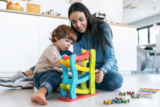 Young beautiful mother playing on the floor with her son in living room at home. stock photo