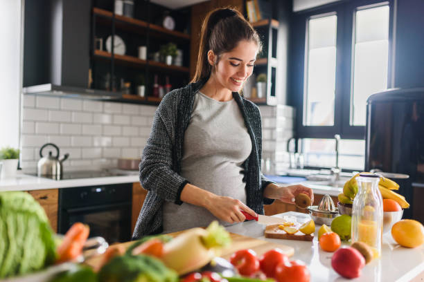 young beautiful pregnant woman preparing healthy meal with fruites and vegetables - woman chopping vegetables imagens e fotografias de stock