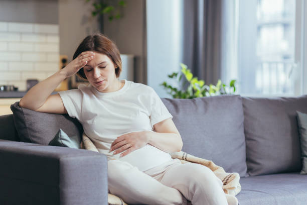 Young beautiful pregnant woman sitting at home on the couch sick, has a headache and nausea Young beautiful pregnant woman sitting at home on the couch sick, has a headache and nausea depression  delivery stock pictures, royalty-free photos & images