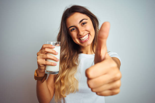 Young beautiful woman drinking a glass of milk over white isolated background happy with big smile doing ok sign, thumb up with fingers, excellent sign  drinking milk stock pictures, royalty-free photos & images