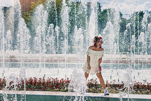Young beautiful woman having fun in the fountain. Horizontal photo