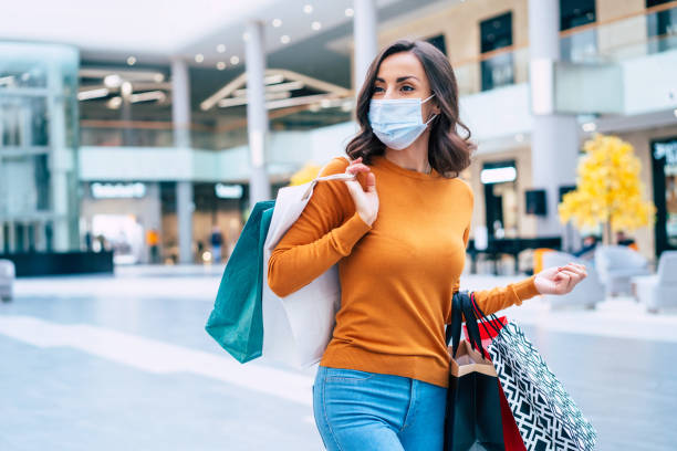 joven mujer hermosa en máscara de seguridad médica con bolsas de compras está caminando en el centro comercial el viernes negro - black friday shoppers fotografías e imágenes de stock