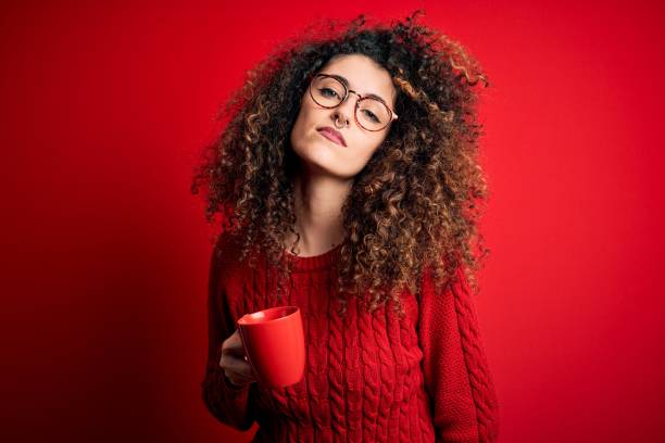 年輕美麗的女人與捲曲的頭髮和刺耳喝紅杯咖啡與自信的表情在聰明的臉思考認真 - curley cup 個照片及圖片檔