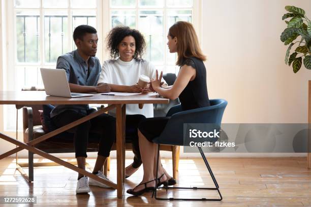 Young biracial couple consulting talking with female designer at meeting