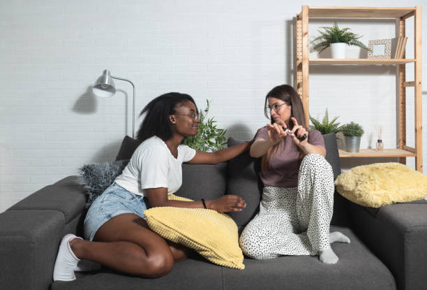 Young black and white lesbian homosexual couple sitting at home make a deal about quitting smoking cigarettes by one woman breaking the cigarette and her happy partner support her in that decision stock photo