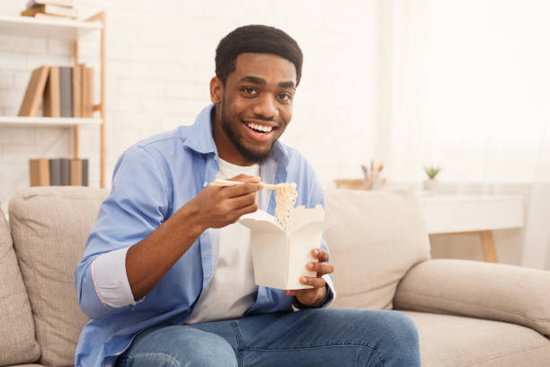 jeune noire nouilles homme manger à la maison - african america man eating chinese food photos et images de collection
