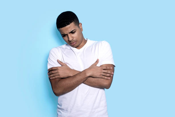 Young black man isolated on blue background while arms crossed and looking down pensive stock photo