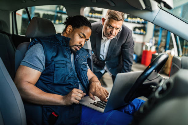 Young black mechanic and his manager using computer in auto repair shop. African American auto mechanic and his customer using laptop while examining car breakdown in repair workshop. auto mechanic stock pictures, royalty-free photos & images