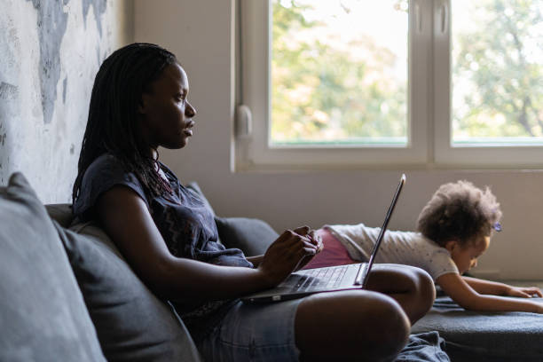 Young black mother sitting in living room with laptop stock photo