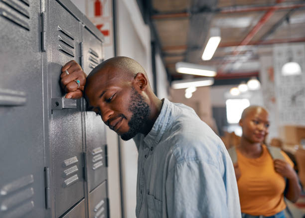 A young black student leans against locker looking stressed as friend walks past stock photo