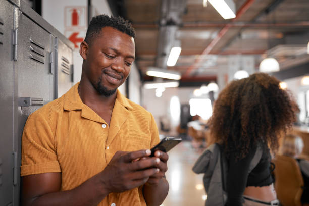 A young black student looks at his phone while a woman walks past on campus stock photo