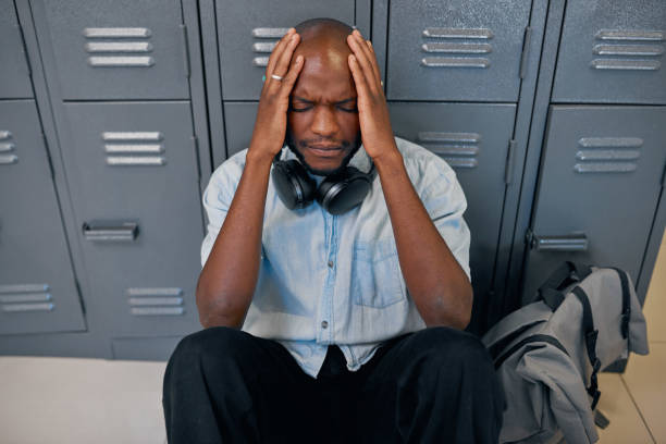 A young black student sits on the floor head in hands, feeling upset at college stock photo