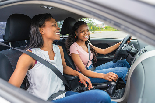 A Young black teenage driver seated in her new car with her mother