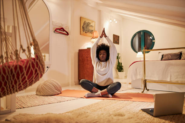 寝室でヨガをしながら瞑想する若い黒人女性 - 夜　ストレッチ ストックフォトと画像