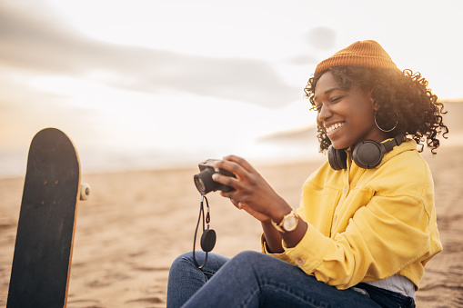 Young black woman sitting on the beach and looking photos on the camera