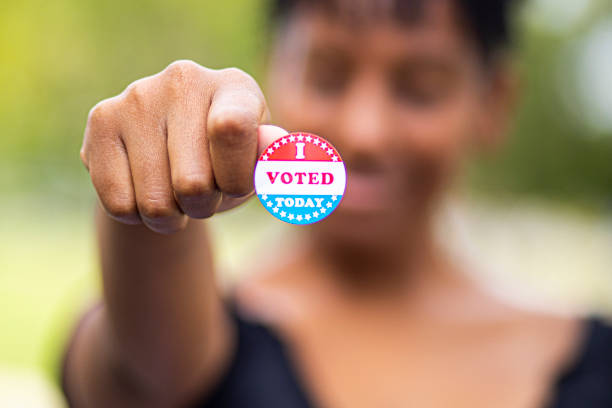 Young Black Woman with I Voted Sticker A young black woman holds an I Voted sticker voting booth stock pictures, royalty-free photos & images