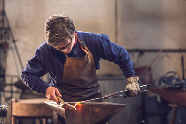 Young blacksmith working with red hot metal Young metalworker or blacksmith working with red hot metal in a workshop with a mallet on an anvil blacksmith stock pictures, royalty-free photos & images