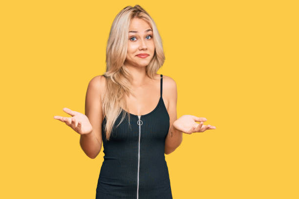 Young blonde girl wearing elegant and sexy look clueless and confused expression with arms and hands raised. doubt concept. stock photo
