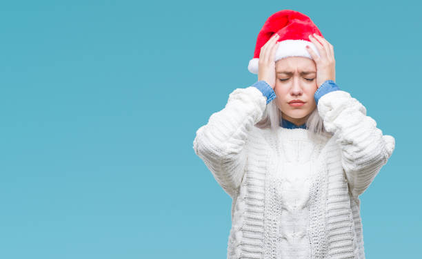 Young blonde woman wearing christmas hat over isolated background suffering from headache desperate and stressed because pain and migraine. Hands on head. Young blonde woman wearing christmas hat over isolated background suffering from headache desperate and stressed because pain and migraine. Hands on head. holiday stress stock pictures, royalty-free photos & images