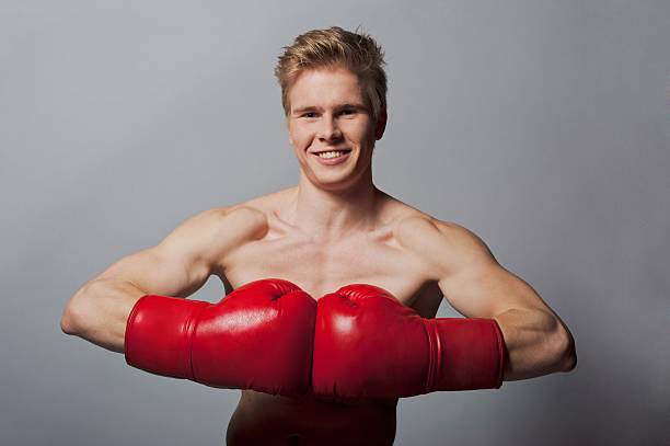 young boxer Portrait of a young blond man with boxing gloves against grey background teenage boys men blond hair muscular build stock pictures, royalty-free photos & images