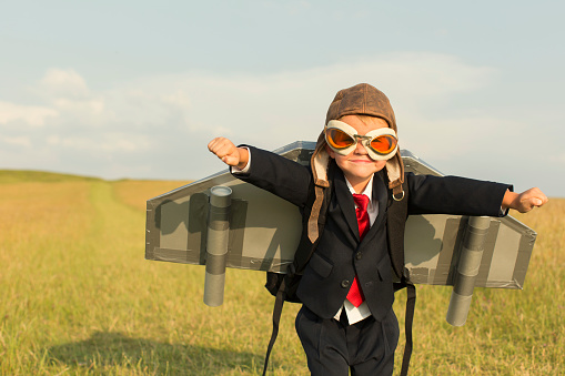 A young British boy is wearing a jetpack standing in a grass field located in the United Kingdom and is ready to take his business into the stratosphere.