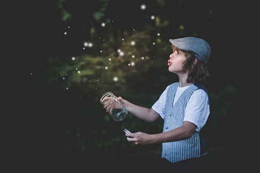 Vintage boy in the evening catching lightning bugs and fireflies in a jar.