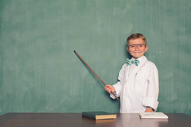 Young Boy Dressed as Scientist Points to Chalkboard stock photo