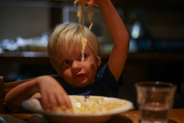 A young boy eats pasta with his hands stock photo
