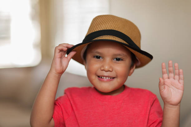 Young boy expressing recognition or gesturing thank you by doing a hat tip and waving his hand with a pleasing smile. stock photo