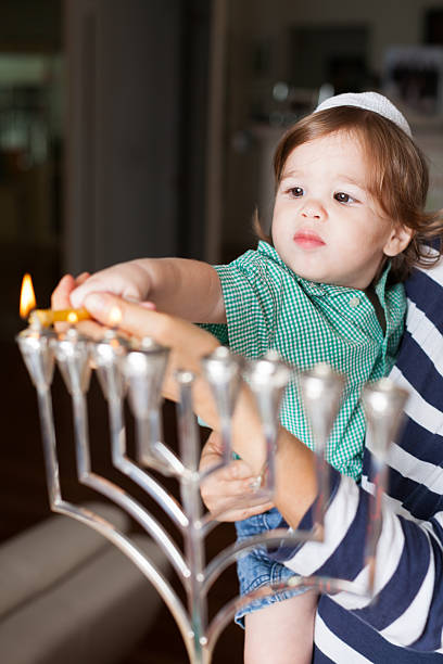Young boy in adult's arms helping to light a menorah stock photo
