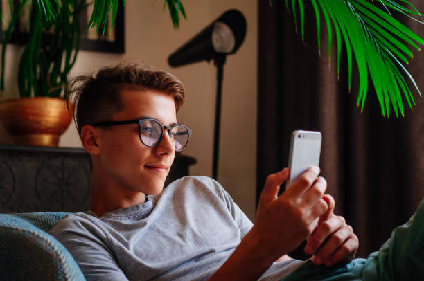 Young boy in glasses using smartphone Generation Z concept. Smiling boy in glasses using smartphone sitting in the chair indoor. generation z stock pictures, royalty-free photos & images