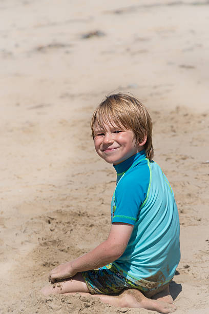 Young boy in sun suit plays with sand on beach stock photo