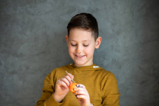 Young boy is coloring Easter egg. Gray background.  easter sunday stock pictures, royalty-free photos & images