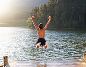 Young boy jumping into lake with arms in the air
