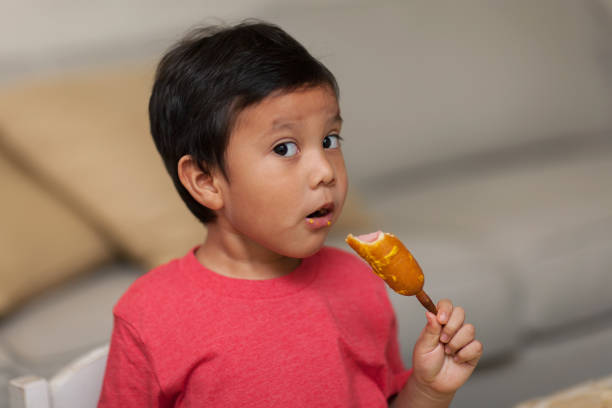 A young boy looks with awe as he takes a bite out of a homemade corn dog, a healthy snack. stock photo