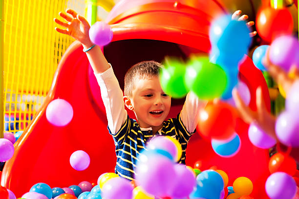 A young boy on a slide playing in a ball pit Little boy in the ball pool indoor playground stock pictures, royalty-free photos & images