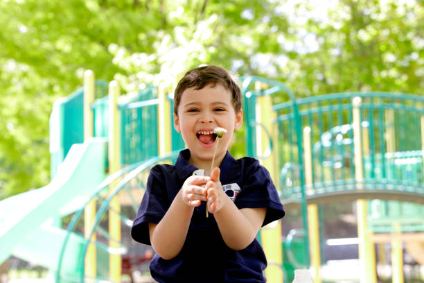 Young boy with autism laughing Playful portrait of a young boy enjoying a spring day at the park. He finds enjoyment in the simple discovery of finding the seed head of a dandelion flower. autism stock pictures, royalty-free photos & images