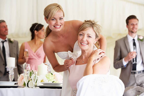 A young bride with her mother at a wedding reception Bride With Mother At Wedding Reception Smiling To Camera mother of the bride dress stock pictures, royalty-free photos & images