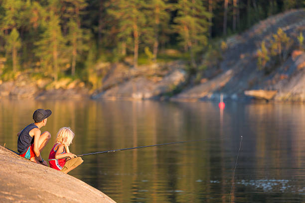 Young brothers fishing from a cliff in sunset. Stockholm Archipelago stock photo