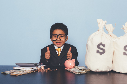 A young boy dressed as a businessman is counting the new business money he has made. Making loads of money for your business requires hard work and a little luck.