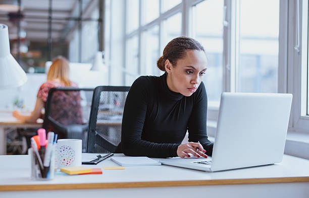 Young business executive using laptop Image of woman using laptop while sitting at her desk. Young african american businesswoman sitting in the office and working on laptop. surfing the net stock pictures, royalty-free photos & images