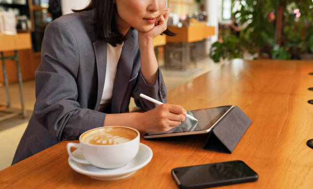 Young business woman using digital tablet working sitting in cafe. Busy young professional business woman using applications on digital tablet pad computer sitting at table in cafe remote working or learning online, writing holding stylus, close up view. Student planner apps stock pictures, royalty-free photos & images