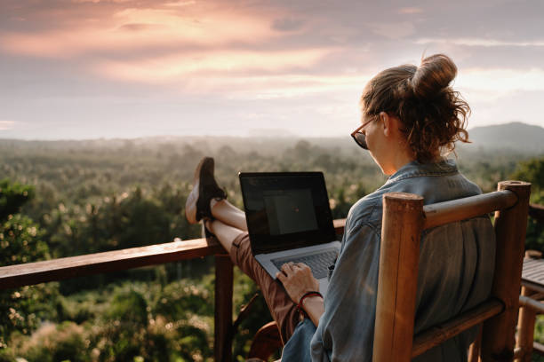 Young business woman working at the computer in cafe on the rock. Young girl downshifter working at a laptop at sunset or sunrise on the top of the mountain to the sea, working day. stock photo
