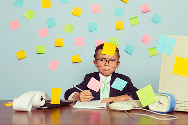 Young Businessman at Desk Covered with Blank Sticky Notes A young businessman sitting at his office computer with pen in hand is completely covered with blank sticky notes. He is forgetting many tasks for his business operations. He wearing a suit and tie and has a frustrated look on his look on his face.   overworked stock pictures, royalty-free photos & images