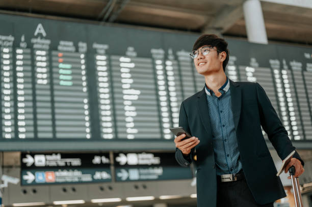 스마트 폰을 사용하여 시간표 화면 보드에서 젊은 사업가. 비행 보드. - business travel 뉴스 사진 이미지