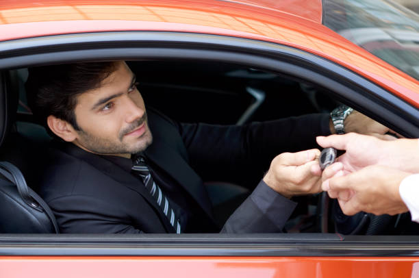 Young businessman in a black suit handling car key to the valet service staff while holding the car wheel. stock photo
