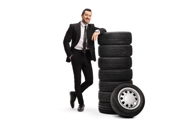 Young businessman leaning on a pile of car tires Full length portrait of a young businessman leaning on a pile of car tires isolated on white background leaning stock pictures, royalty-free photos & images
