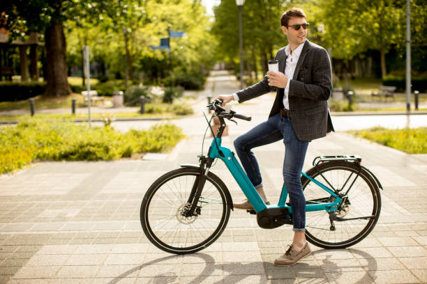 Young businessman on the ebike with takeaway coffee cup Handsome young businessman on the ebike with takeaway coffee cup electric bicycle stock pictures, royalty-free photos & images