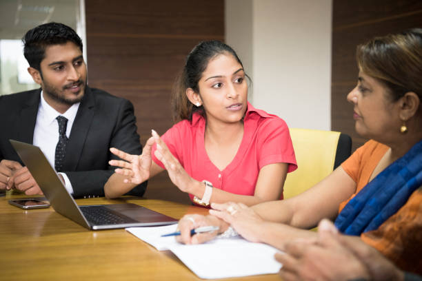 Young businesswoman gesturing and explaining in meeting with laptop Male and female colleague watching and listening, woman in her 20s sitting at table with laptop and serious expression sri lanka women stock pictures, royalty-free photos & images